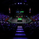 a spotlight shines on a snooker table in the middle of a darkened auditorium as two snooker players get ready for a match