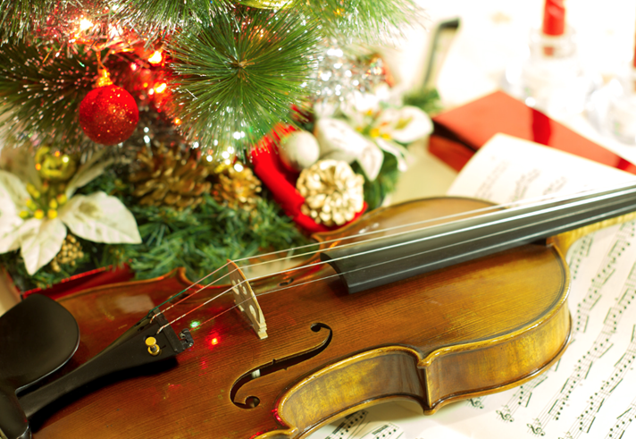 A violin on a table covered in sheet music and a Christmas ornament off to one side.