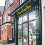 Exterior view of Porter Book Shop on a residential street, featuring a dark green storefront with large windows displaying posters and books. A chalkboard sign on the pavement reads ‘Book Shop Open’, and red‑brick terraced houses line the street in the background.