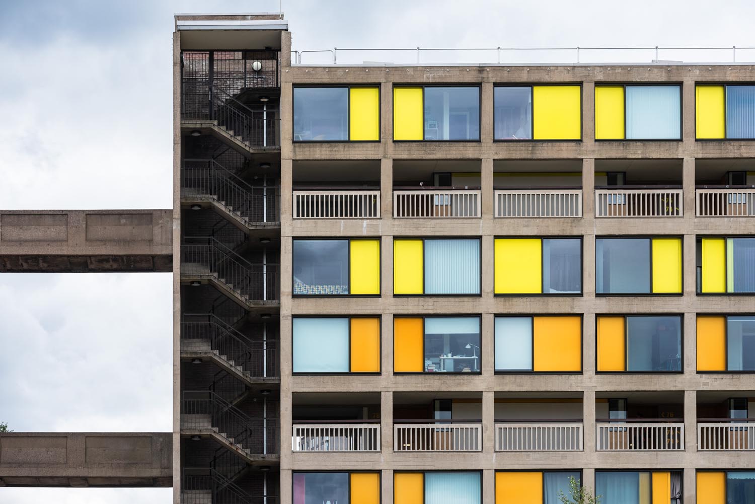 A tower block with rows of alternating windows and bright yellow or orange panels. At one end is a tower with stairs running all through it.
