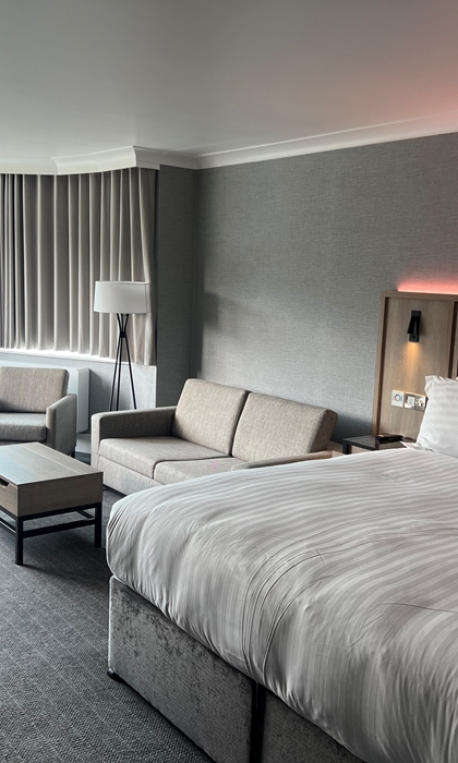 Modern double bedroom with seating area and ambient mood lighting.