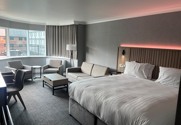 Modern double bedroom with seating area and ambient mood lighting.