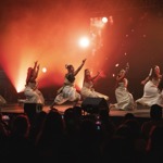 A group of singers performing on an orange lit stage.