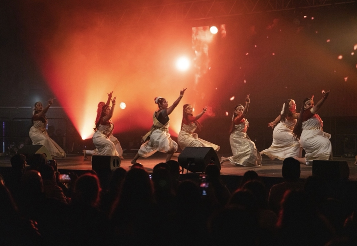 A group of singers performing on an orange lit stage.