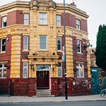 Rutland Arms exterior. The building is red and mustard brick, with grey sky in the background and two bicycles and street art to the right of the building.