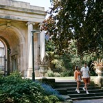 Couple walk down steps with the grand archway at the entrance to Sheffield Botanical Gardens in the background