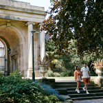 Couple walk down steps with the grand archway at the entrance to Sheffield Botanical Gardens in the background
