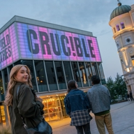 Sheffield Theatres’ Crucible building glowing pink at dusk, showing people arriving for an evening performance in the city centre.