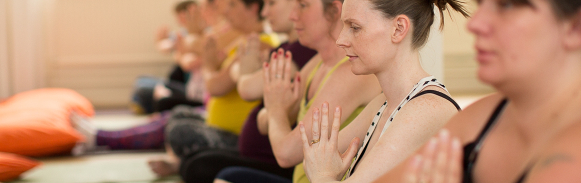 A row of people, sat on the floor, in a yoga class.