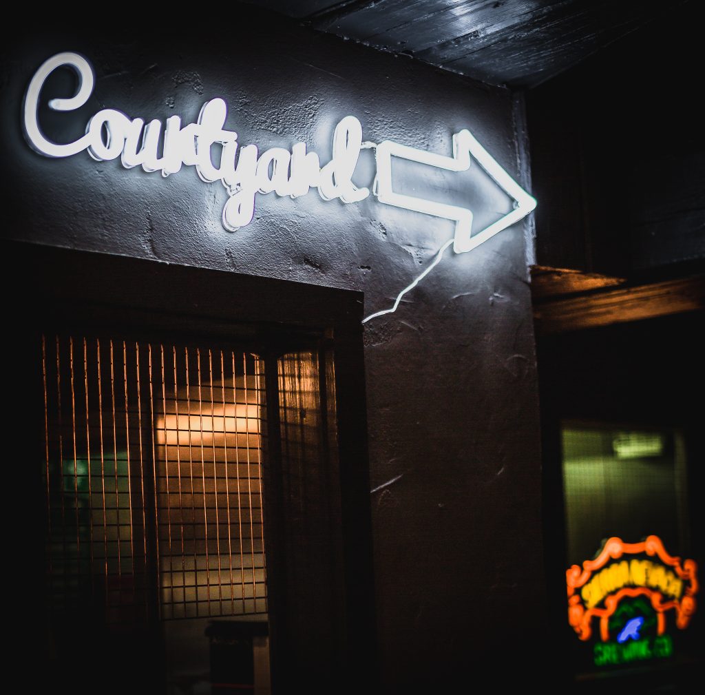 A white neon sign that reads 'Courtyard' on the wall at Monk Bar.