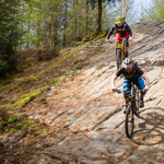 Two people on mountains bikes ride down a rocky slope in the countryside.