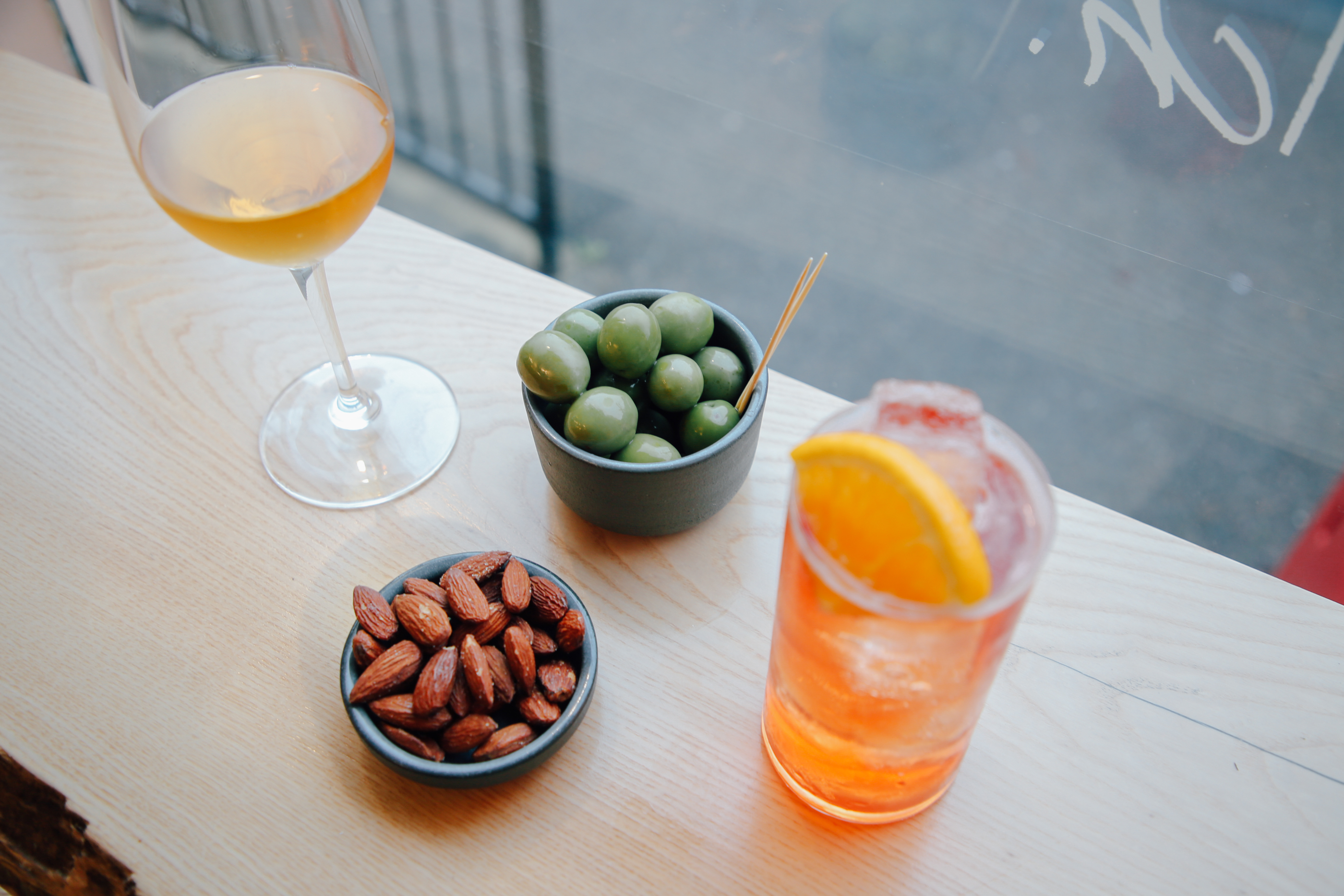 A bowl of olives, a bowl of nuts, a glass of wine and a cocktail on a table.
