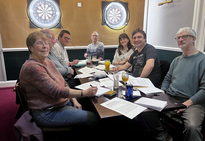 A group of people sat round a table, writing letters.