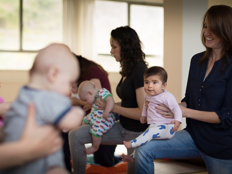 A group of mothers, holding their babies, in a yoga class.