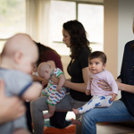 A group of mothers, holding their babies, in a yoga class.