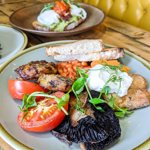 Three plates of food on a wood table in a booth.