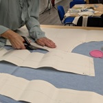 A close-up of someone cutting a clothes pattern out of blue cloth.