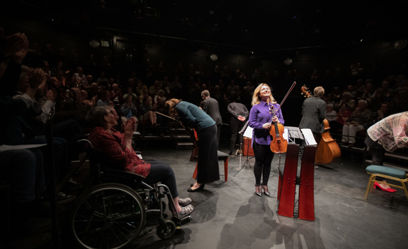 A string quintet are stood in a circle, bowing, as a crowd applauds them.
