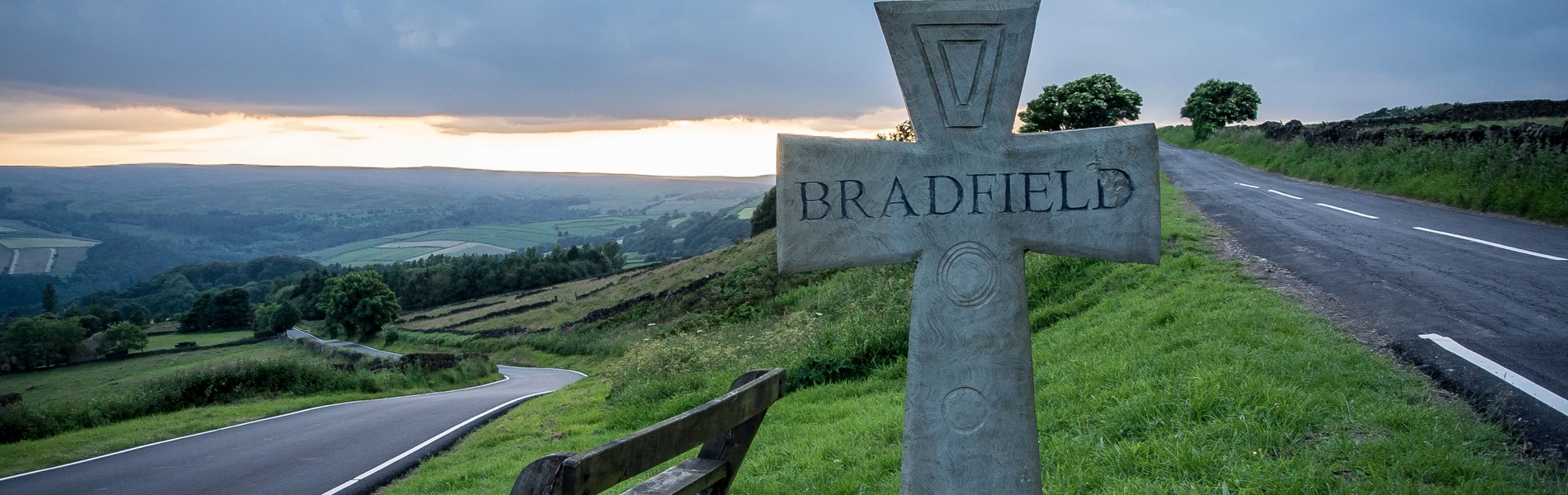 On a grass verge between two roads stands a stone cross with the word 'Bradfield' carved into it.