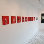 A row of portraits, with striking red backgrounds, at the Cupola Gallery.