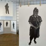 Multiple black and white art works displayed on walls and free standing mesh grids at an art exhibition.