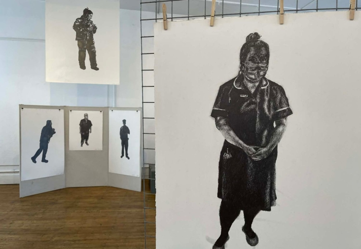 Multiple black and white art works displayed on walls and free standing mesh grids at an art exhibition.