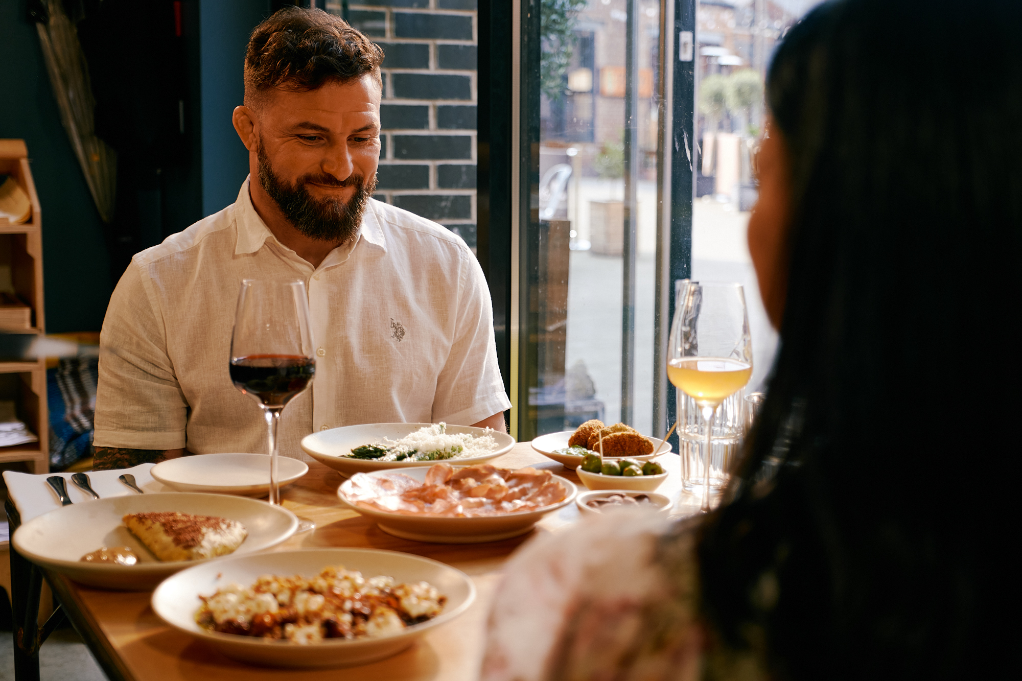 A couple, sat at a table full of food, enjoy a meal out together.