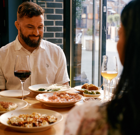 A couple, sat at a table full of food, enjoy a meal out together.