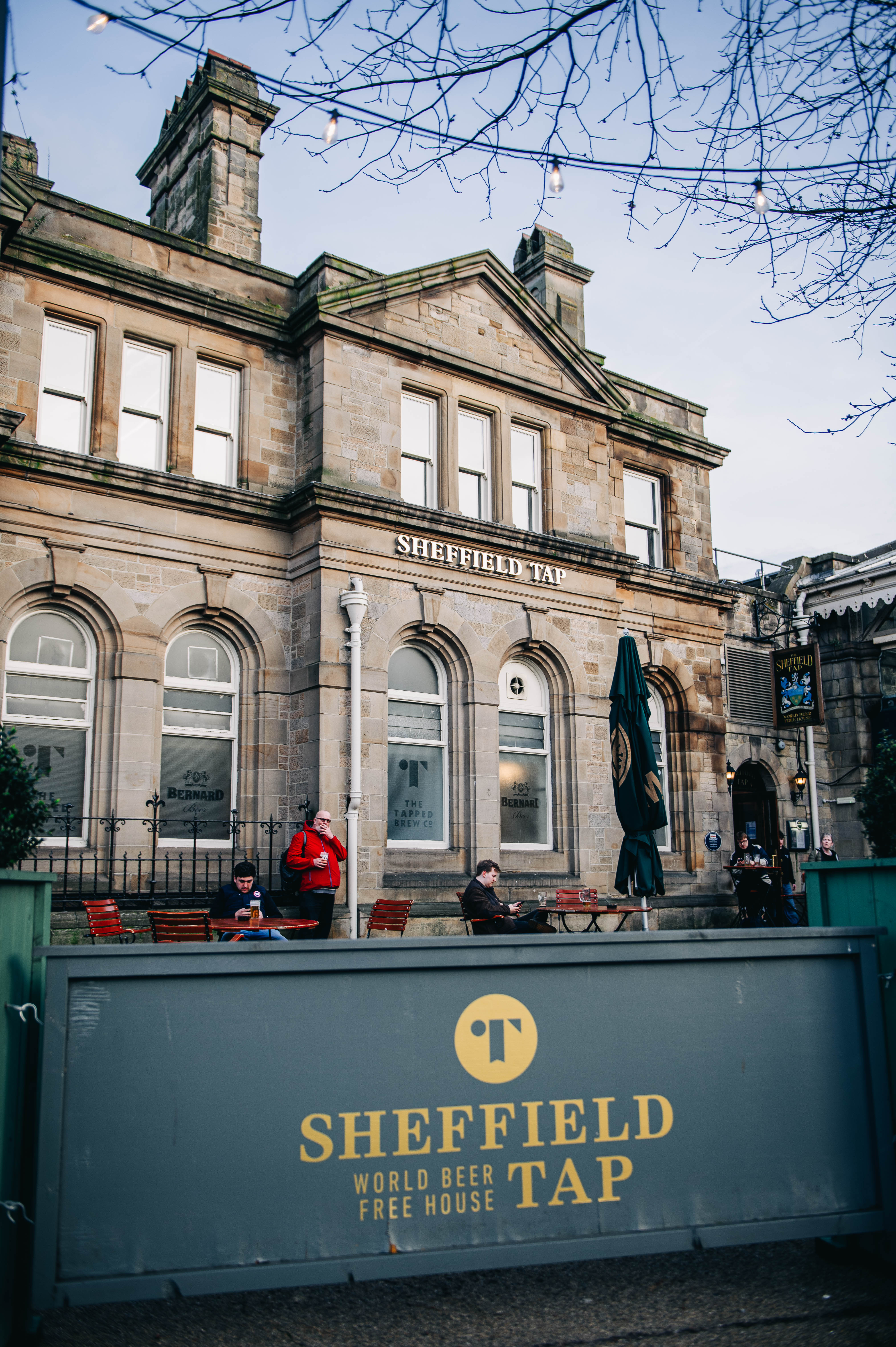 Sheffield Tap exterior outside Sheffield Train Station. A few men are dotted about the outdoor seating area.