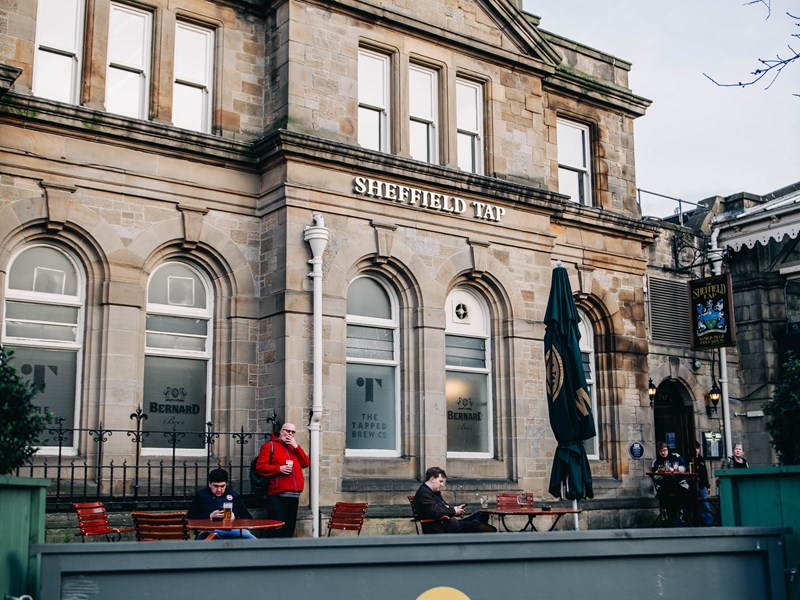 Sheffield Tap exterior outside Sheffield Train Station. A few men are dotted about the outdoor seating area.