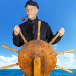 A man, with a pipe in his mouth, stands behind a ships wheel, steering a boat.