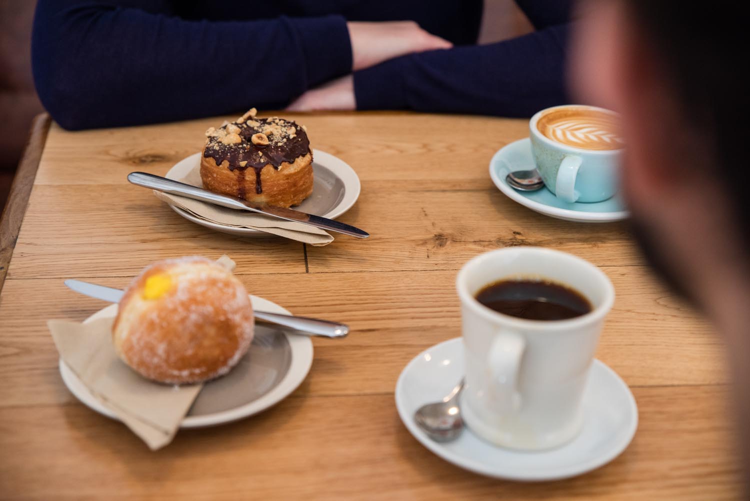 A wooden table with two cups of coffee and two doughnuts.