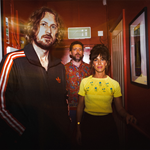 A picture of the band which consists of three individuals, who are standing in a corridor, with vintage lightening