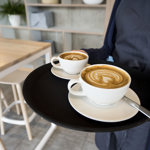 Two cappuccinos being carried on a tray.