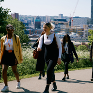 A group of people walk through a park. Behind them you can see Sheffield city centre.