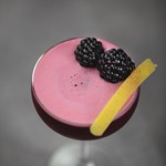 A red cocktail with two blackberries on top.