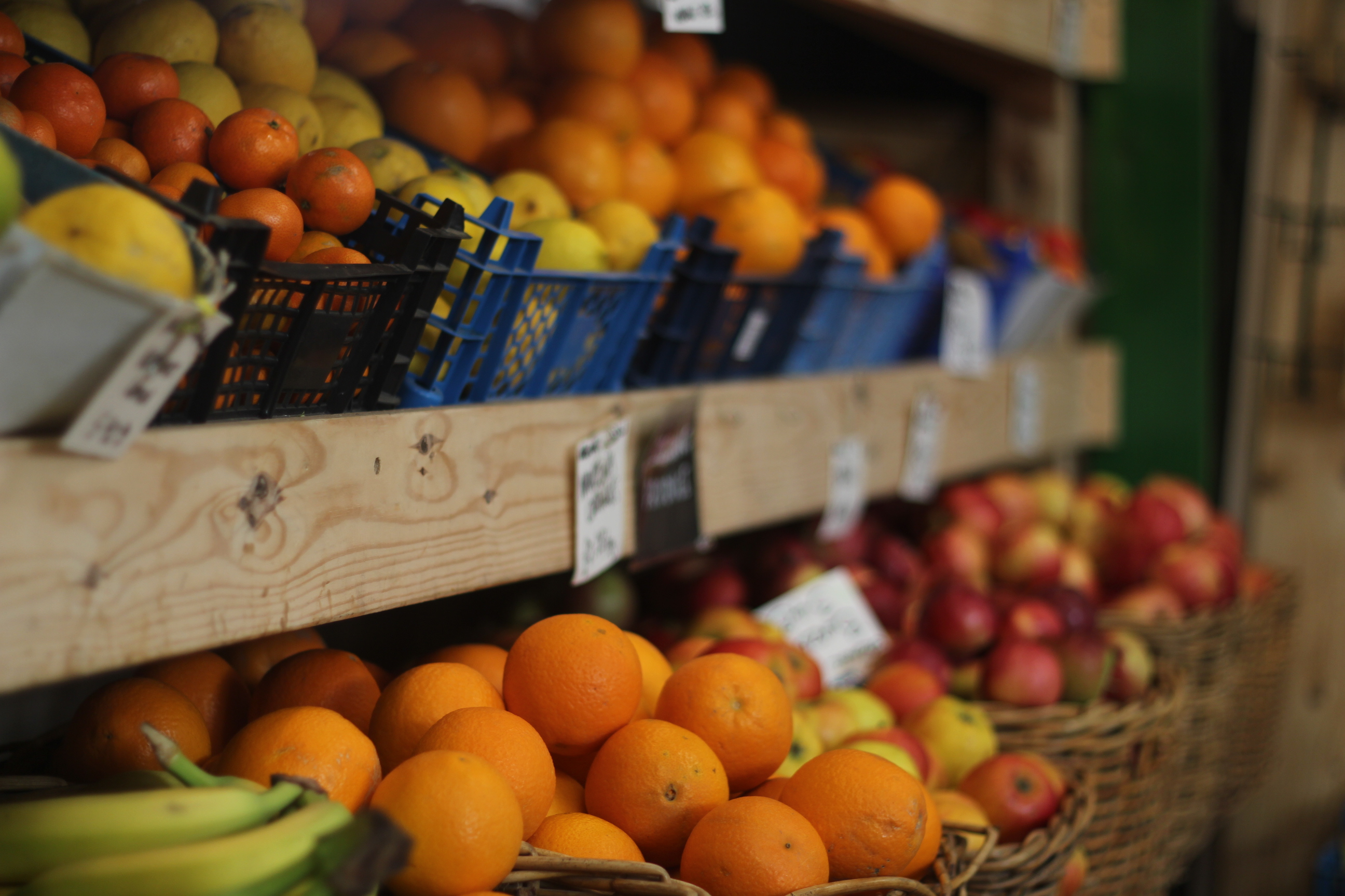 Wooden shelving with baskets full of oranges, apples, bananas and lemons.