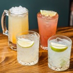 Four cocktails on a wooden table, including citrus drinks and a pink drink with ice.