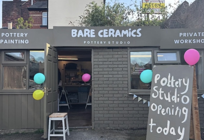 Exterior of Bare Ceramics pottery studio with open doors, colourful balloons, and a sign reading “Pottery Studio Opening Today,” showing the entrance and workshop space inside.