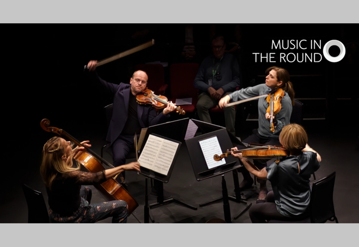 Classical musicians are sat in a circle, facing each other, performing.