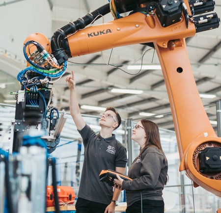 Two technicians monitor a robot working in an advanced manufacturing plant.