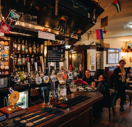 Rutland Arms interior. The bar is at the forefront, with groups of people in the background sat talking at drinking.