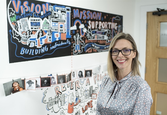 A smiling woman stands in front of a wall that is filled with information posters.