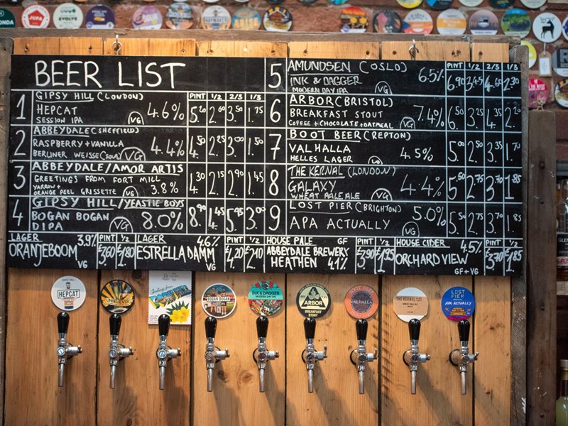 Beers taps and a blackboard with beers listed and prices.