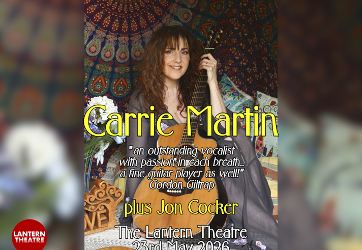 The artist Carrie Martin sat on cushions, holding her guitar.
