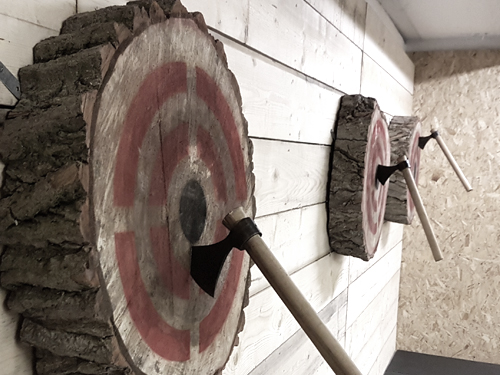 Three wooden targets on a wall, each with a throwing axe in the bullseye.