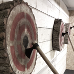 Three wooden targets on a wall, each with a throwing axe in the bullseye.