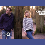 A man and a woman stand in a wooded area.