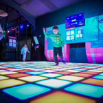 Adults and children dance on a light up disco floor.