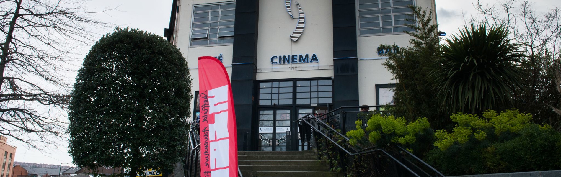 Showroom Cinema in front of grey skies, with a bright pink Sheffield Adventure Film Festival flag to the front left of the building